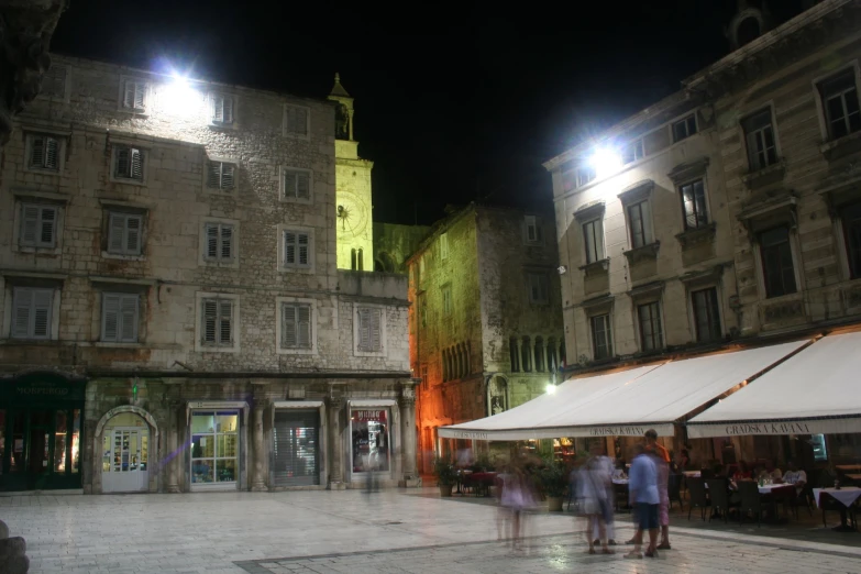 people walking around a square at night with many buildings in the background