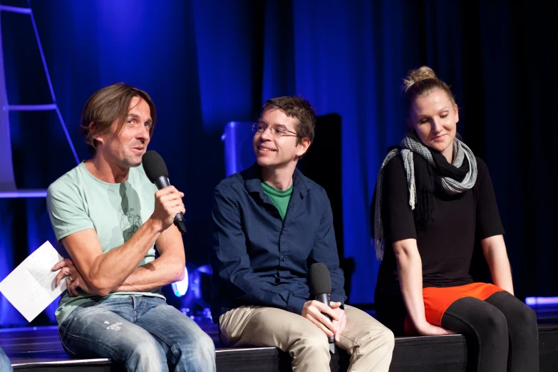 four people sit on a couch and a man is speaking into a microphone