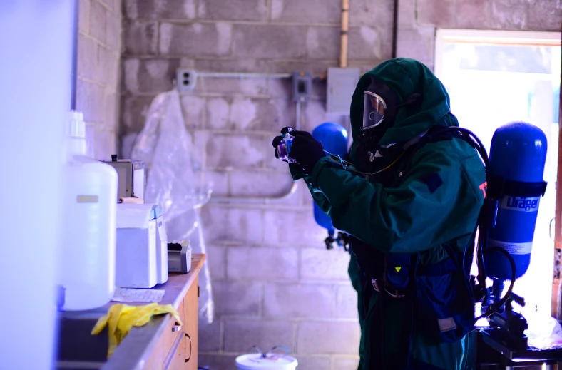 a man in a green and blue outfit is wearing a gas mask while working on a machine