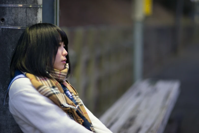 the woman is sitting on a bench wearing a scarf