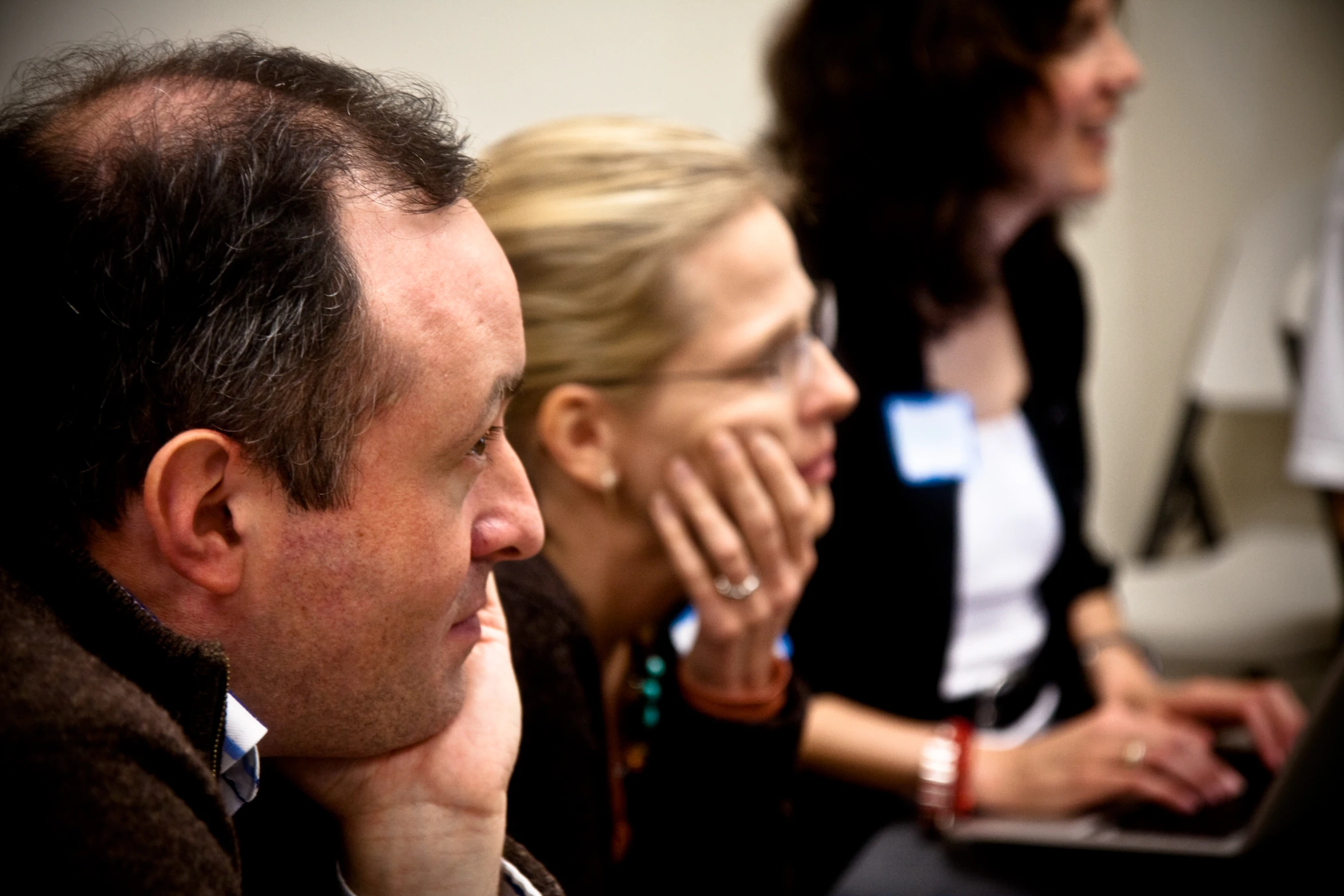 three people are smiling while looking at a laptop