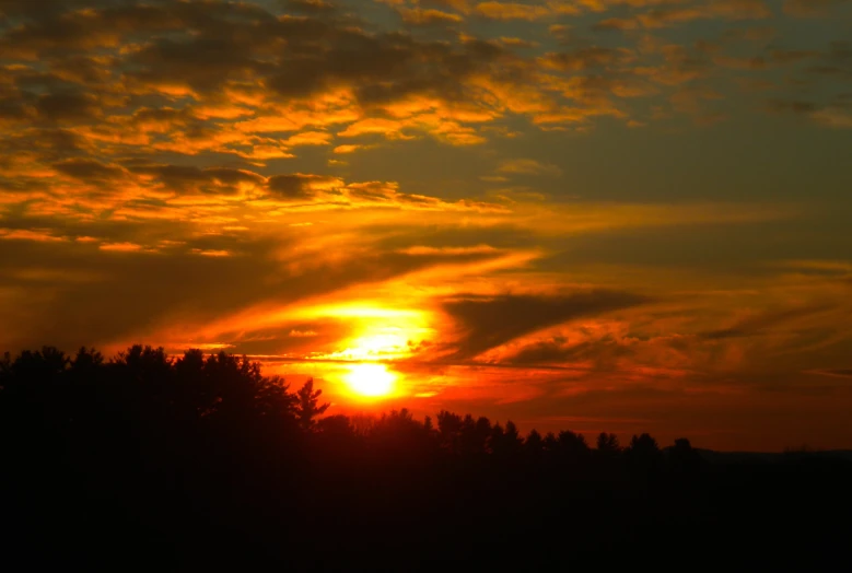 the sun is setting over the clouds over the trees