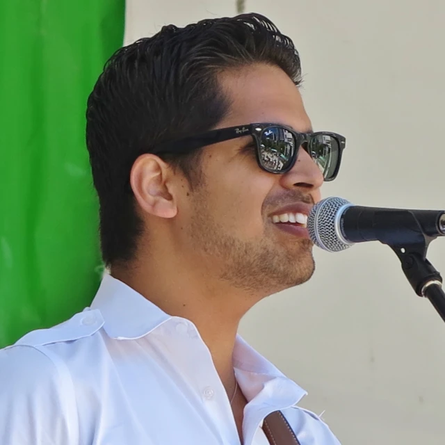 a man wearing sunglasses while singing into a microphone