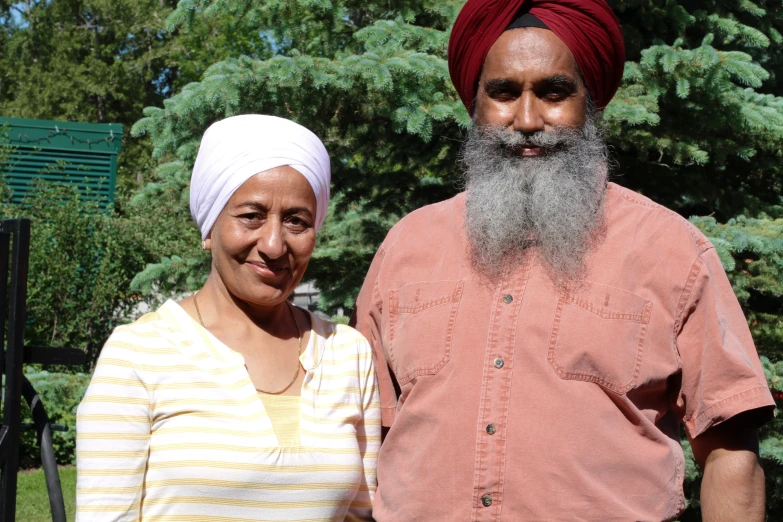 a man with a beard stands next to a woman wearing a red turban