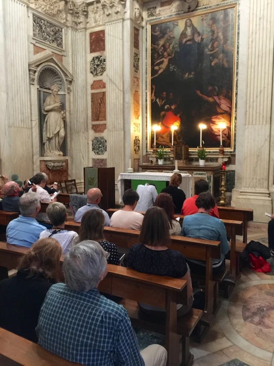 people sit in pews at the alter in front of a painting