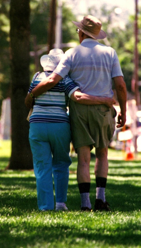 an older man and young woman stand back to back in a park