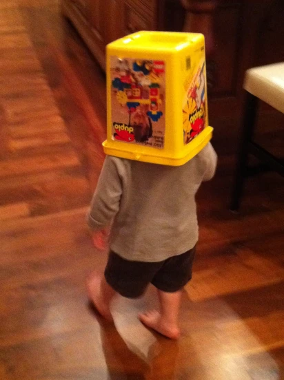 a little  wearing a plastic toy box on his head