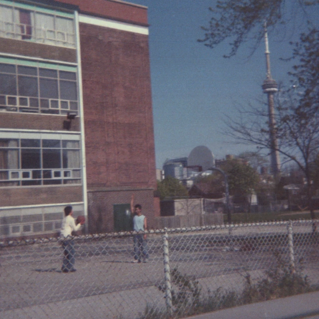 children play in a fenced lot in front of a building