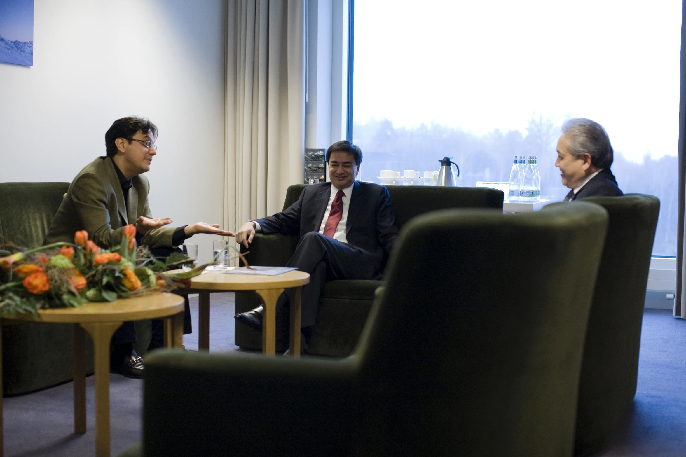 two men sit on couches as one sits in a chair