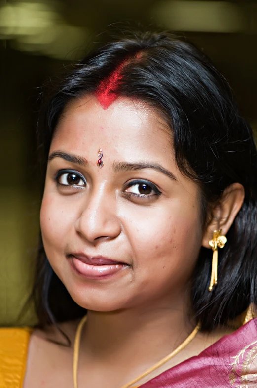 a smiling woman with dark hair and a red painted foreheadband