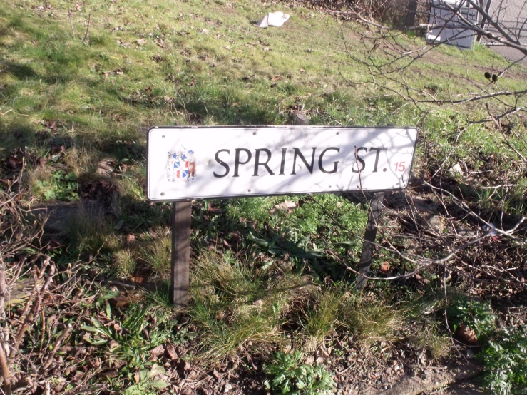 a white street sign sitting in the grass near a tree