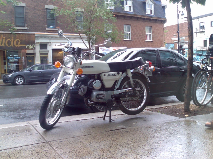 a motorcycle parked beside a car in the rain