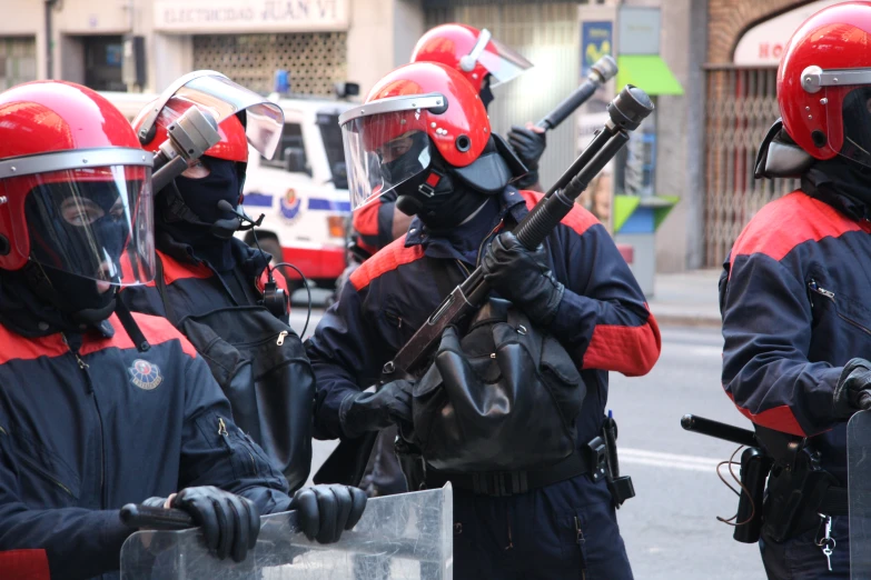 men with red helmets and gun in front of a police car