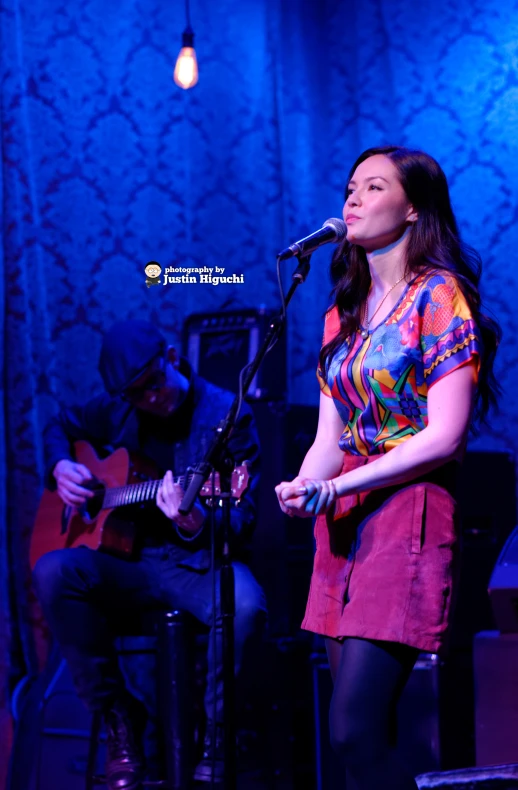 woman singing into a microphone while holding guitar