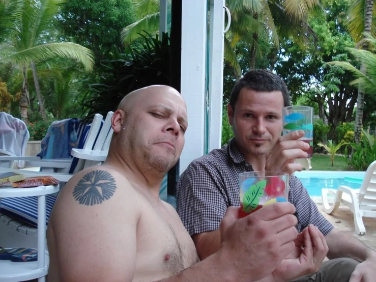 a pair of men hold up glasses on a pool deck