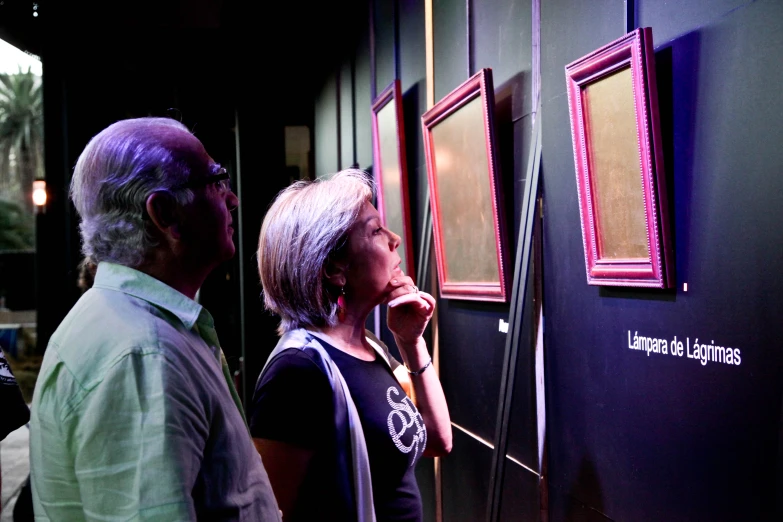 three people looking at two wall paintings one has a pink and blue display