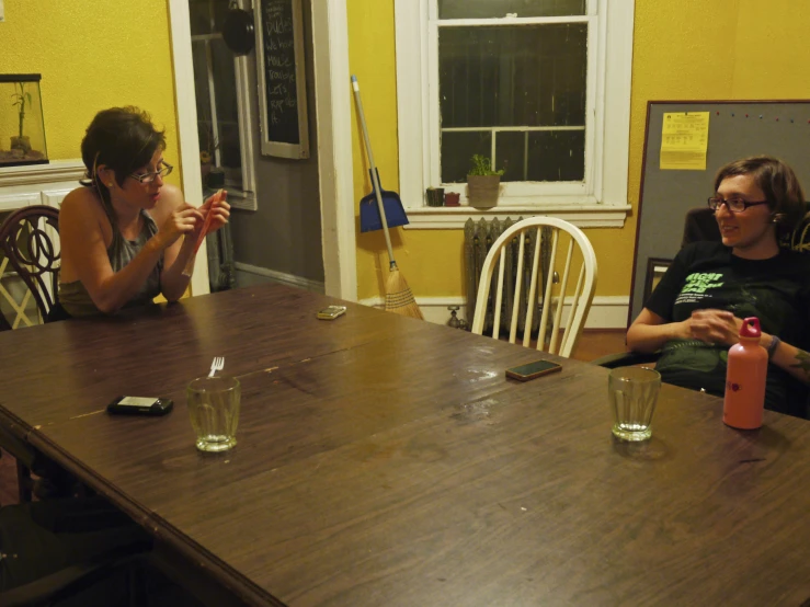 two people sitting at a table and drinking from glass