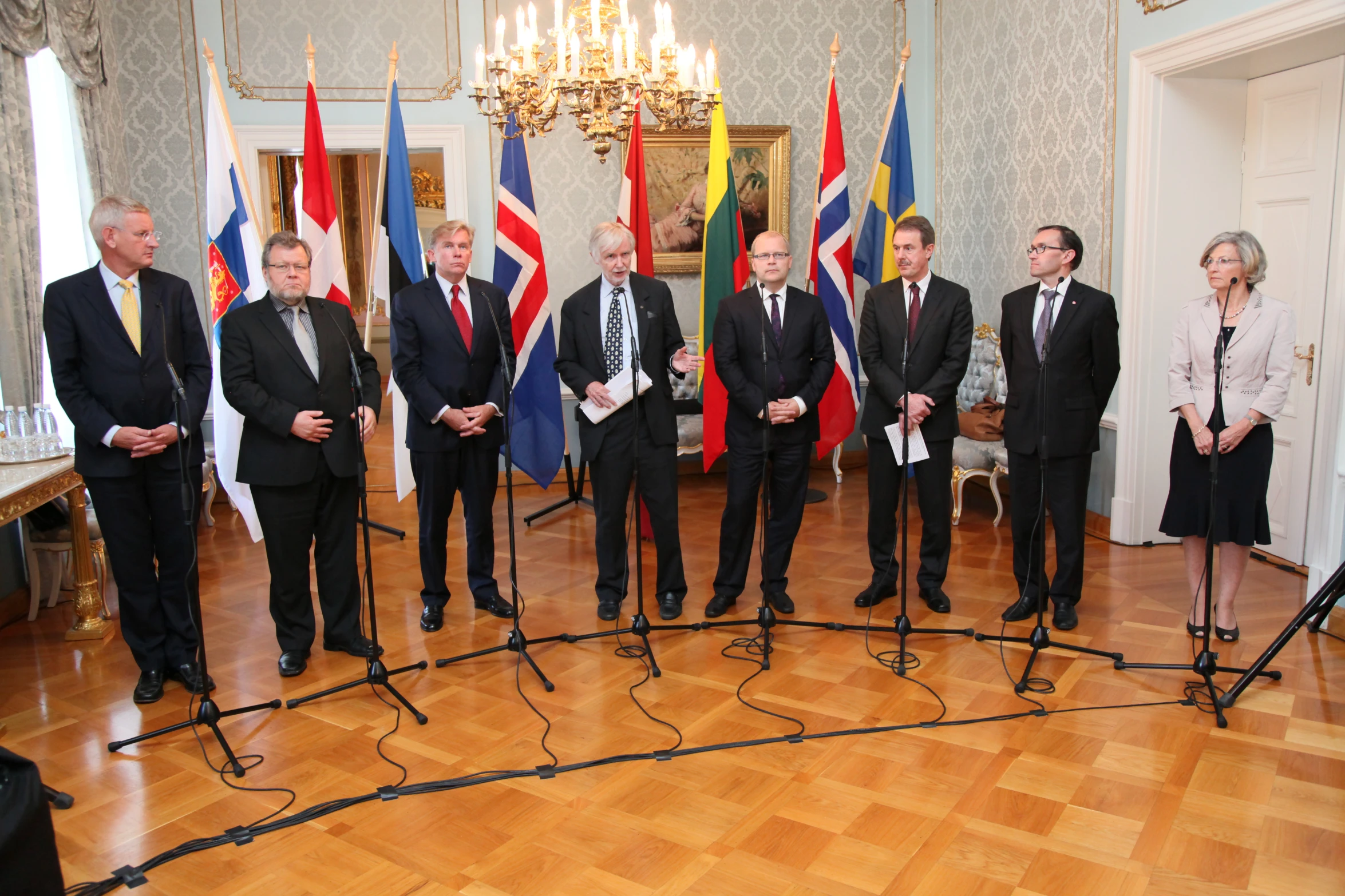 five people stand around a microphone with flags