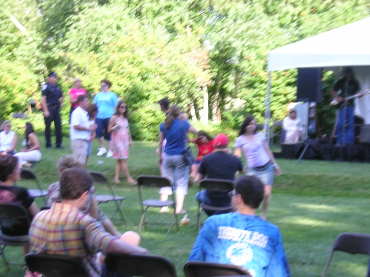 a group of people standing and sitting in chairs on grass