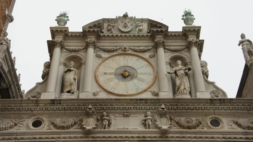 a clock on the side of a building with statues around it