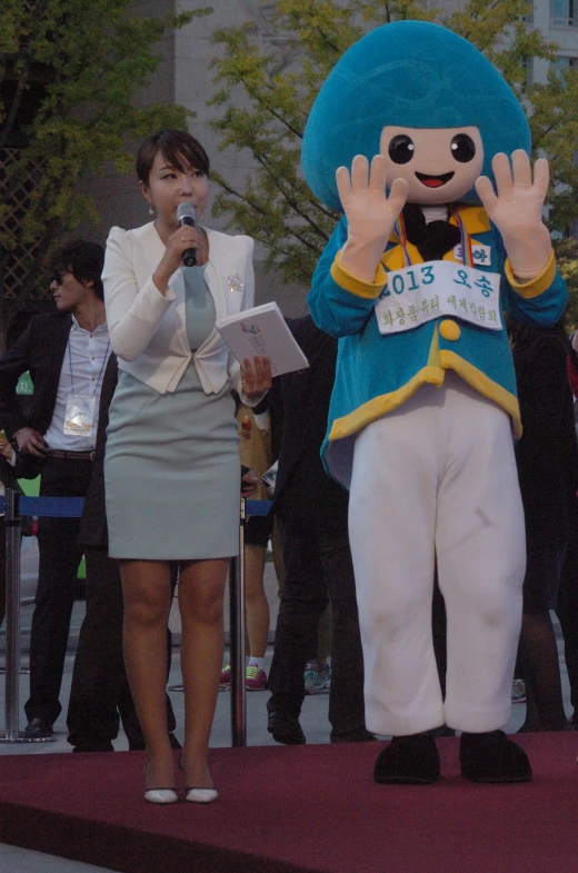 a woman in blue is standing in front of a mascot with her hands up