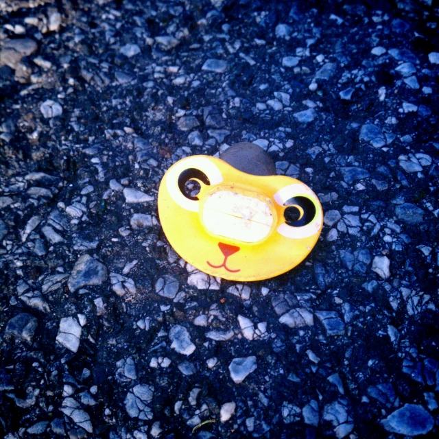 small yellow toy dog on graveled surface next to rock