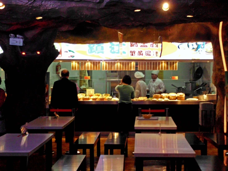 people are standing around a restaurant counter with various dishes on it