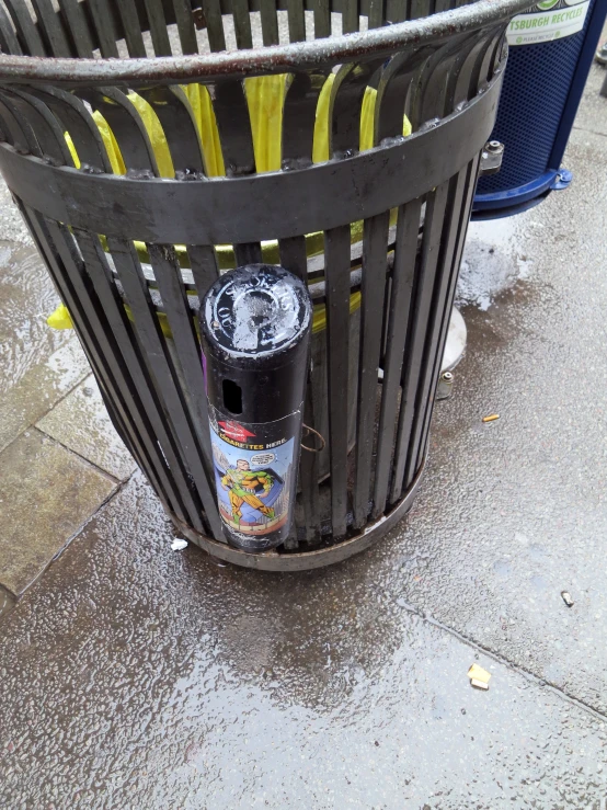 a garbage can on the sidewalk with a can of beer on it