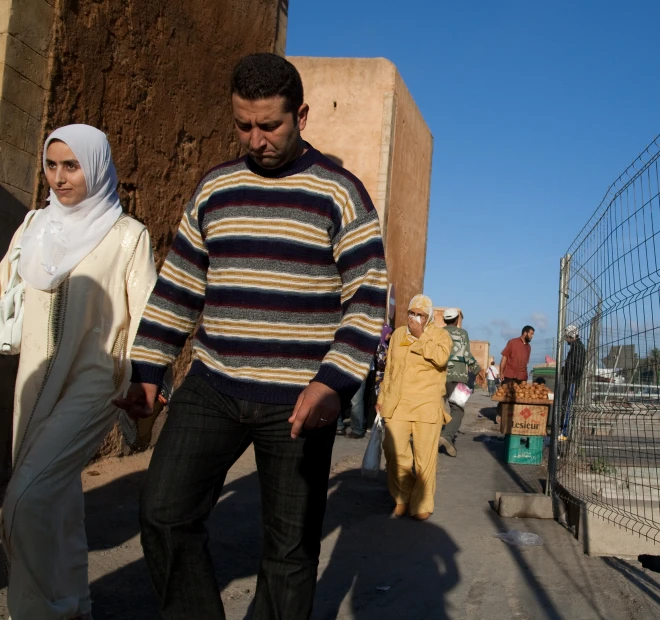 a man walking down a street past a women in head covering