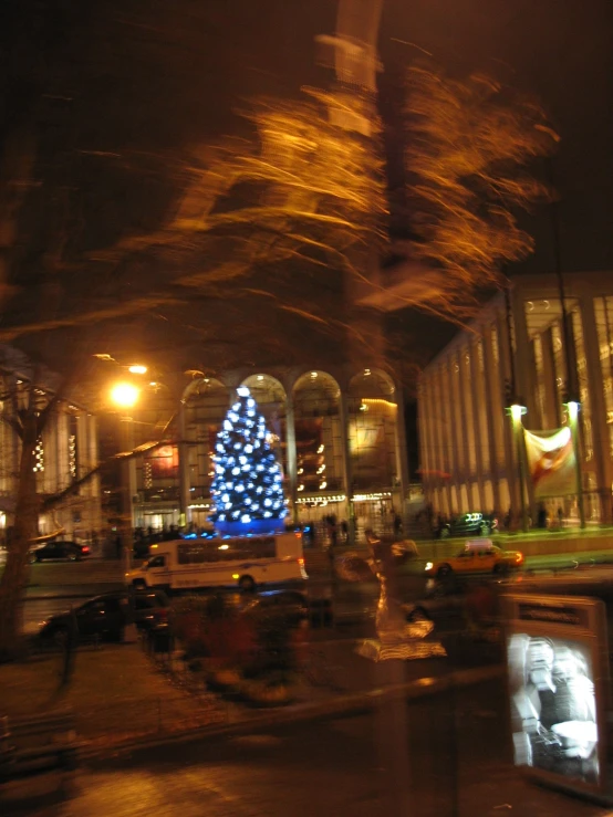 a large christmas tree in front of a tv in the center of an urban setting