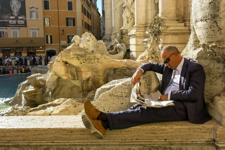 a man sitting on the edge of a fountain in a public area