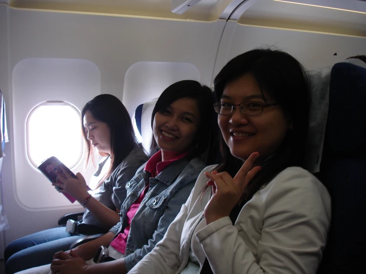 three asian women sit together in seats on an airplane