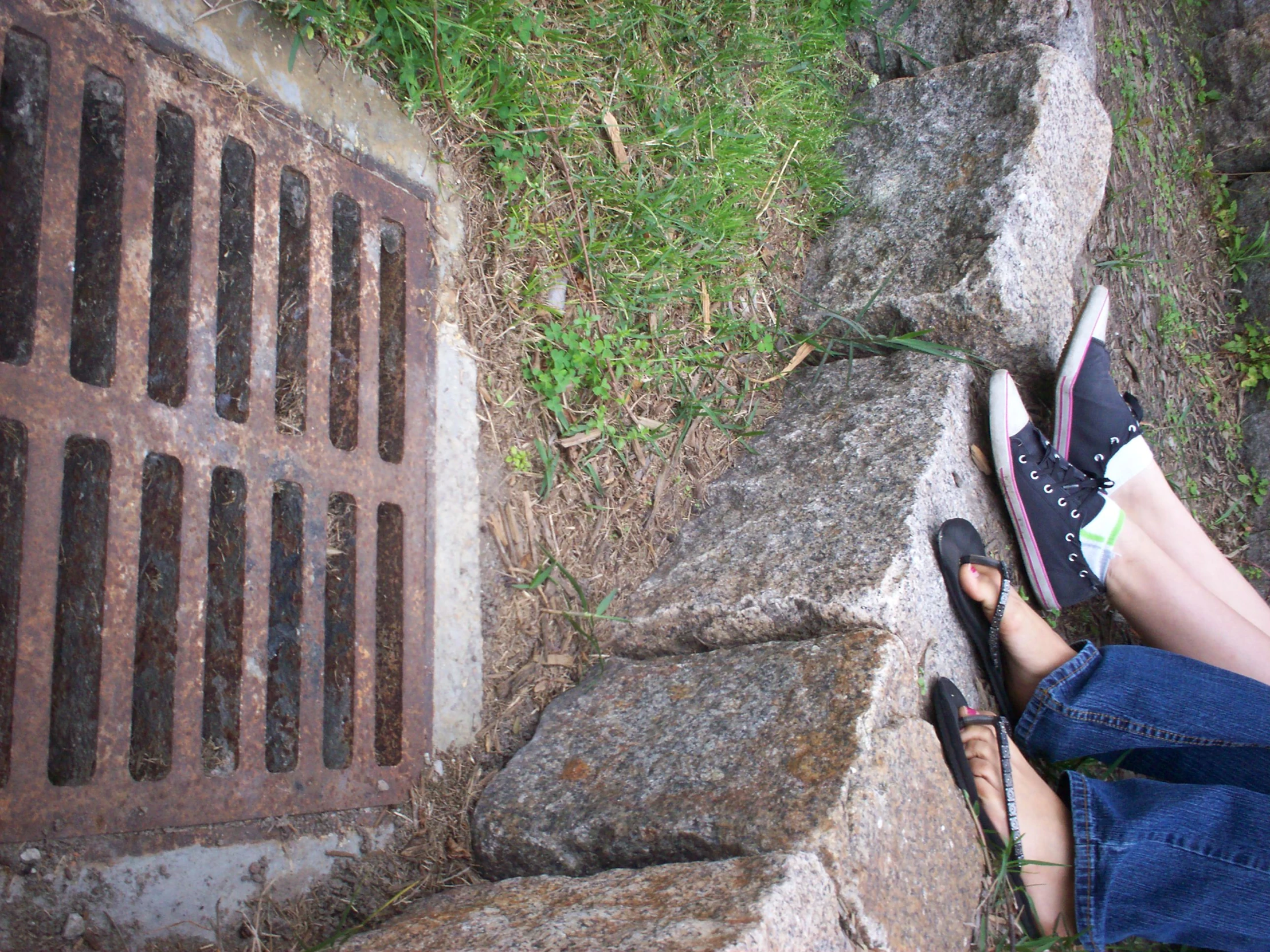 a woman's feet standing on some stones beside a hole