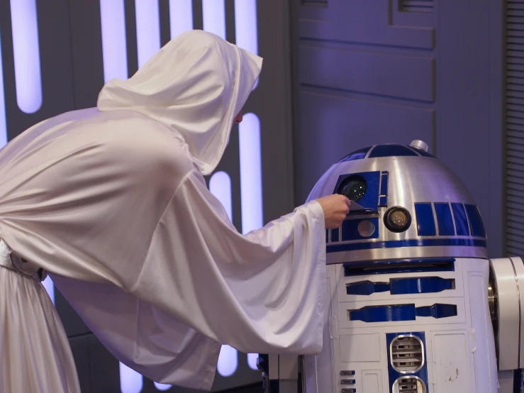 a person in white robes leaning on a c - 3po statue