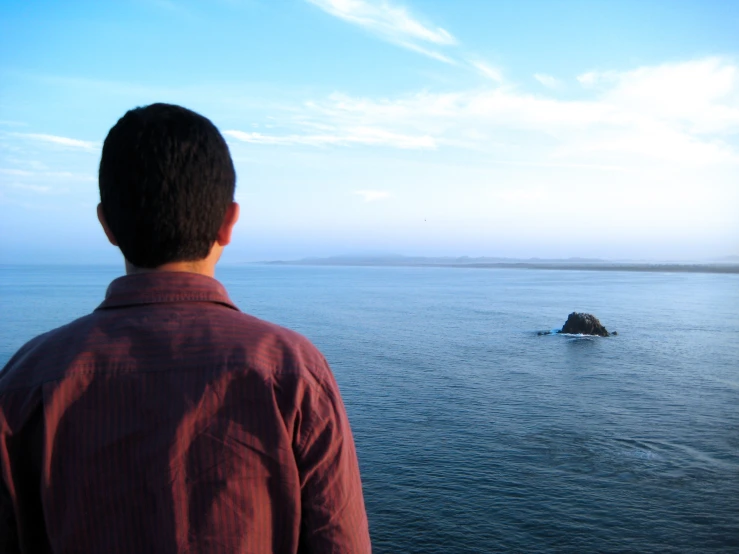 a man standing on the shore of the sea watching an island