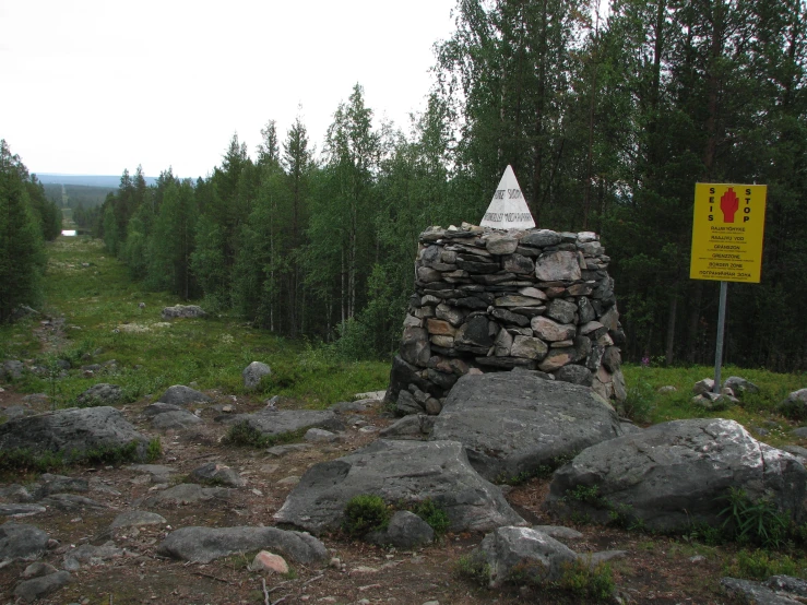 a stone wall by a yellow sign on the side of a dirt road