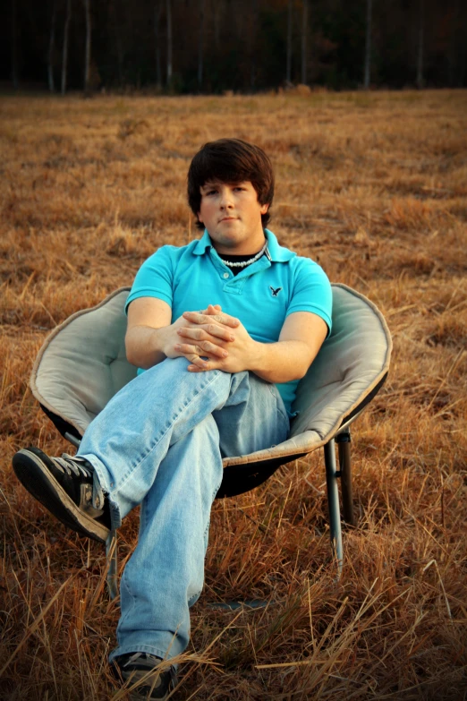 a man in blue shirt sitting on chair in grassy field