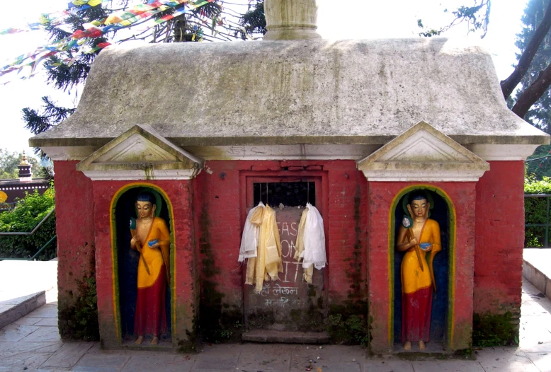 a couple of statues sit in doorways by some trees