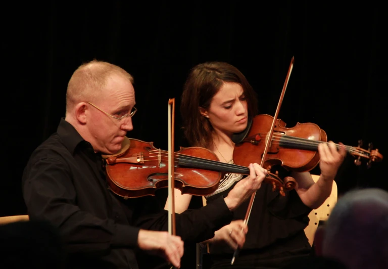 two people are playing violin on stage