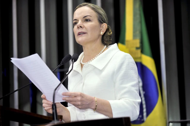 a woman in a white shirt stands at a podium speaking into microphones