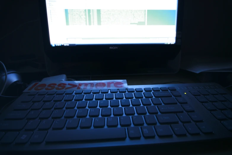 a computer keyboard lit up on a desk with a laptop monitor
