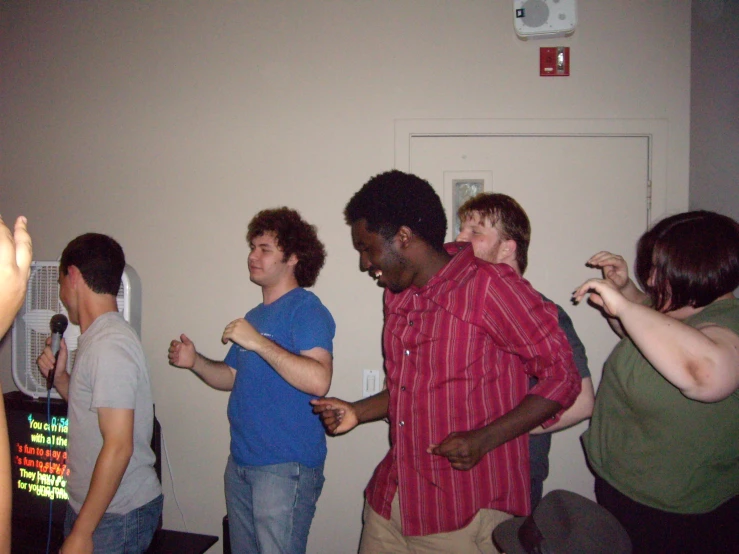 several people standing in a room with one guy playing a video game