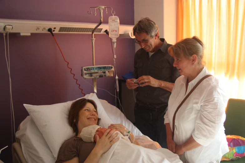 three people looking at a monitor and a baby laying in bed