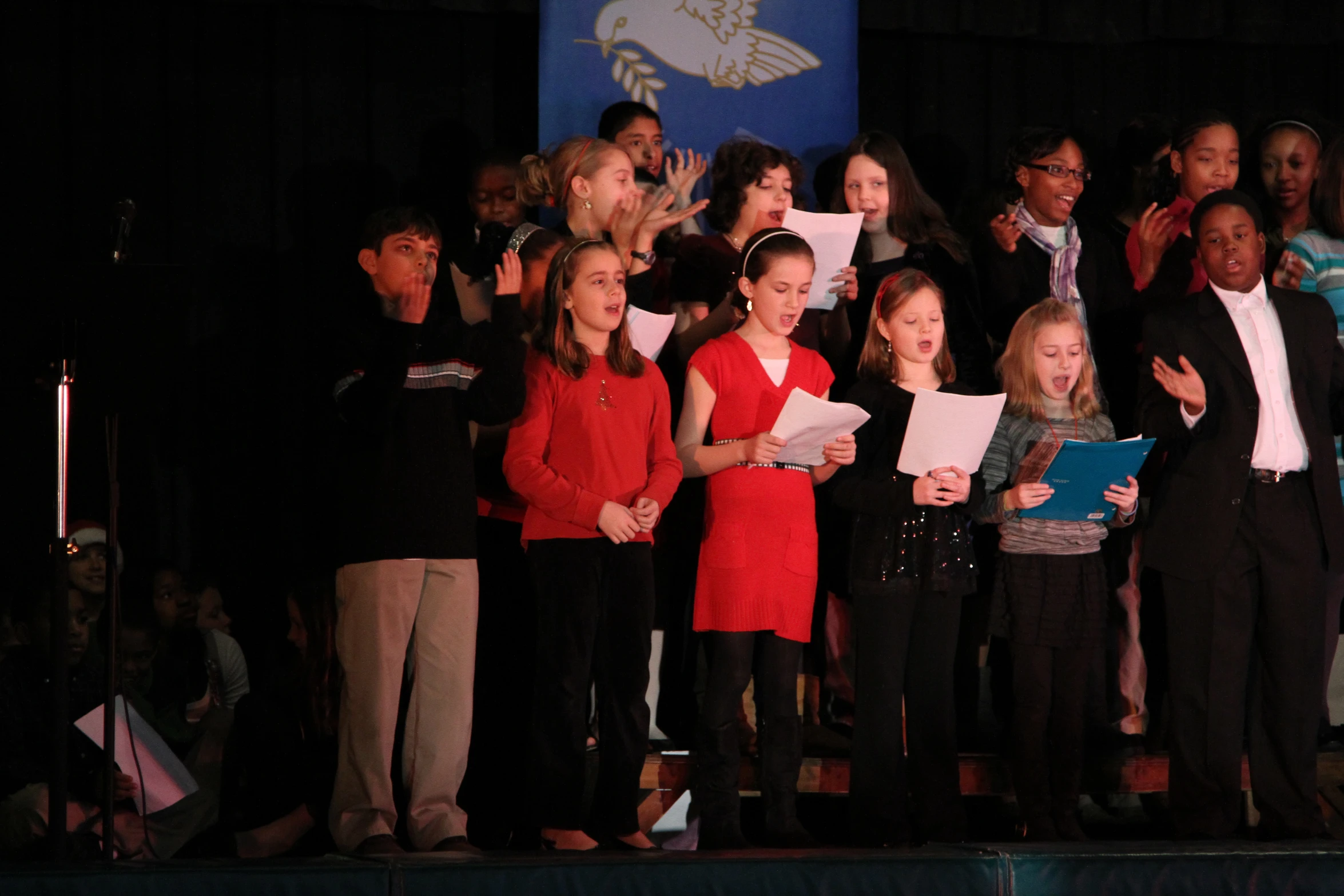 several children singing at a concert with their hands in the air