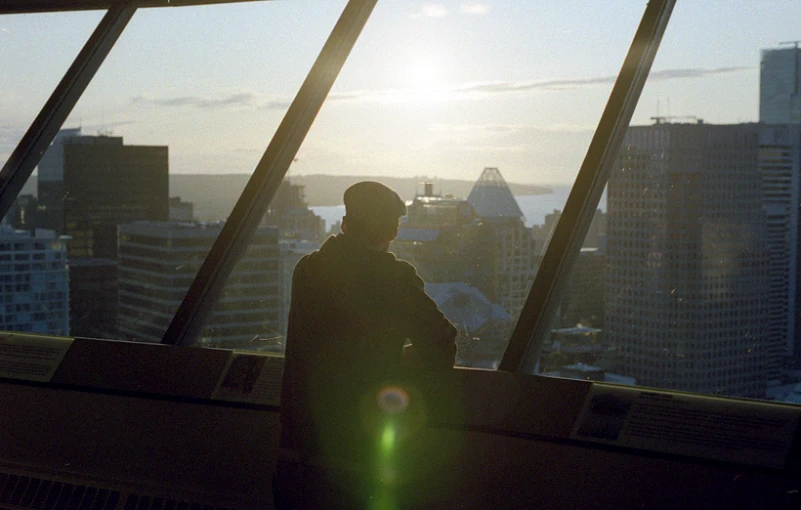 man standing in front of window overlooking the city at sunset