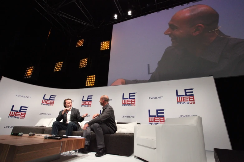 two men sitting on a table talking to each other