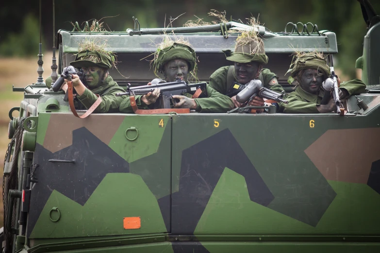 three men in army fatigues on top of a green vehicle