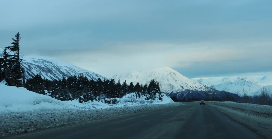 a large snowy hill with some trees and clouds in the sky