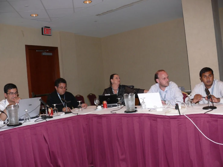 several men sitting at a conference table with their laptops