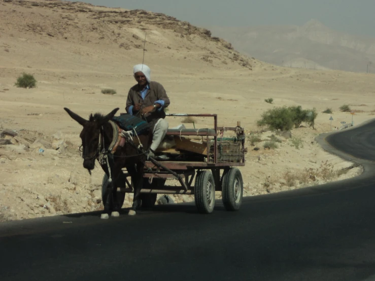 a man in headgear driving a horse carriage down the road